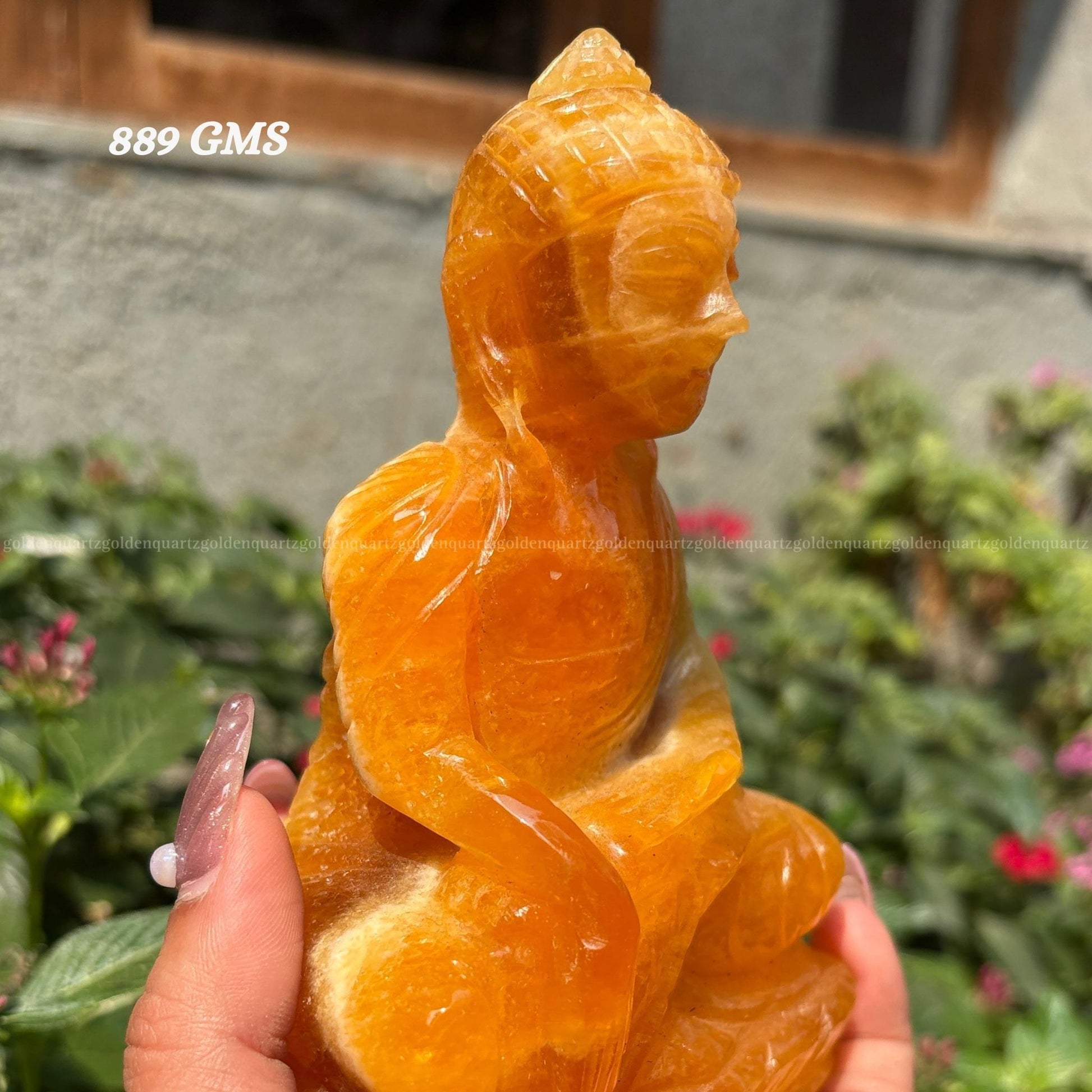 Carved orange fruit sculpture held by a hand with a blurred garden background, yellow calcite buddha statue Golden Quartz