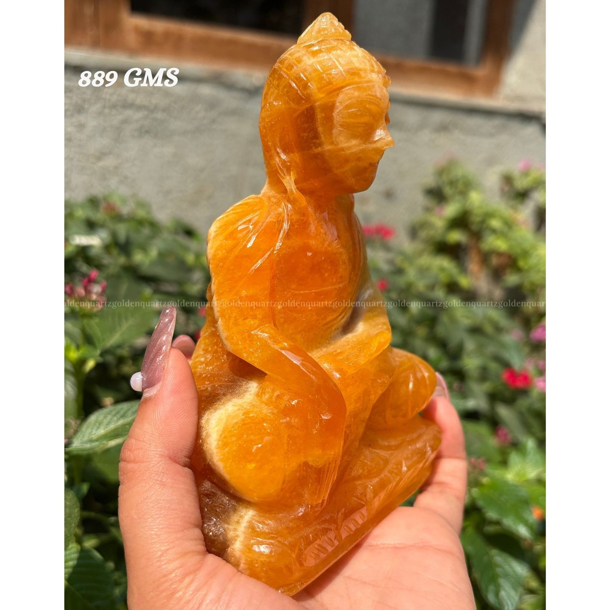 Hand holding a crystal Buddha statue with a blurred garden background Golden Quartz 