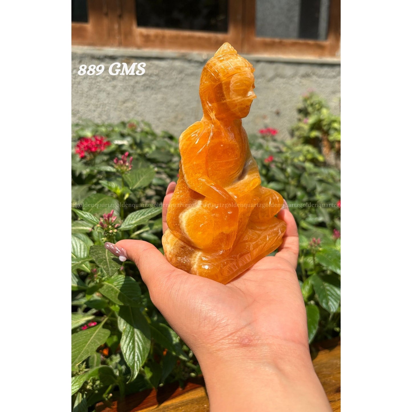 Hand holding a yellow stone Buddha statue with plants in the background Golden Quartz The Crystal Hub