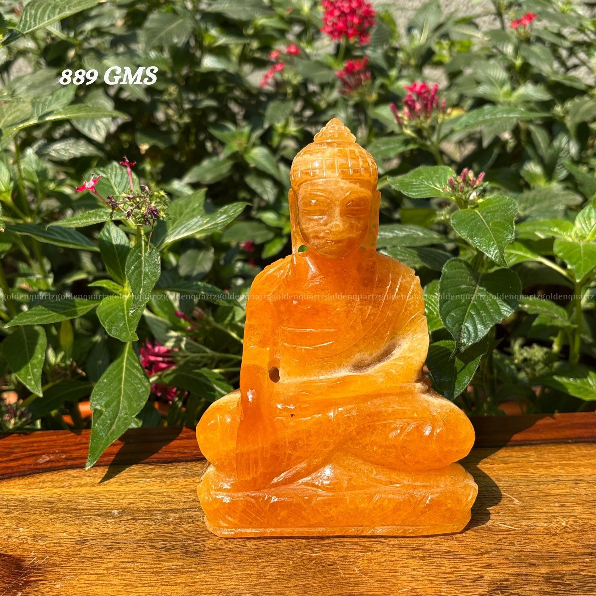 Orange stone Buddha statue on a wooden surface with green foliage in the background